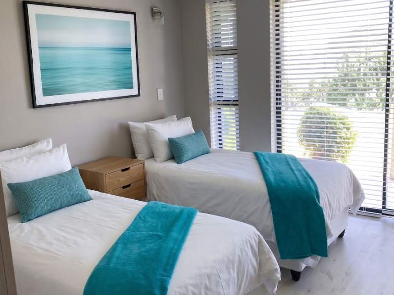 A well-maintained bedroom featuring light laminate flooring, crown molding, and large sliding glass doors with venetian blinds allowing for ample natural light.
