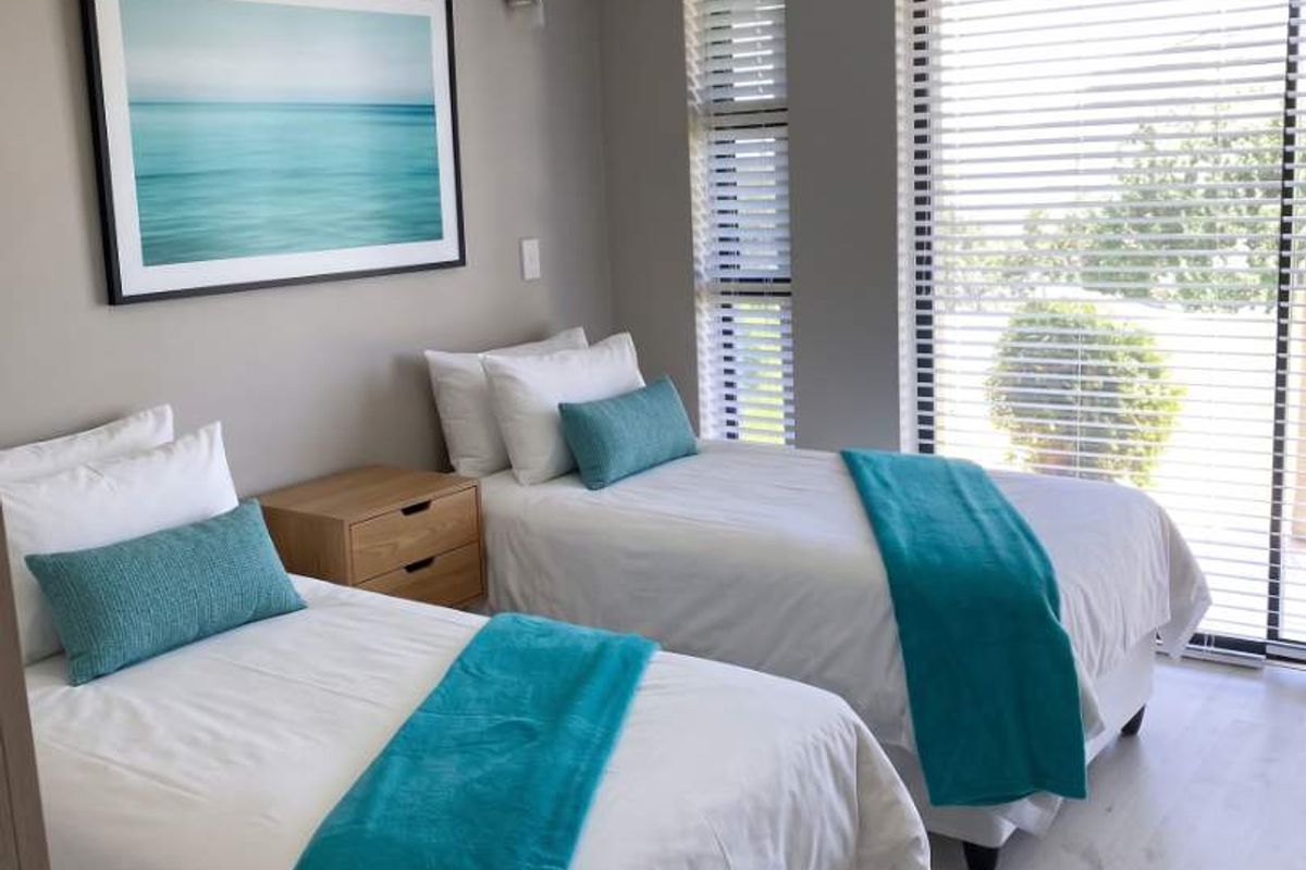 A well-maintained bedroom featuring light laminate flooring, crown molding, and large sliding glass doors with venetian blinds allowing for ample natural light.
