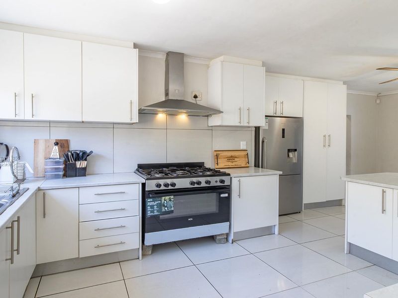 A bright, modern kitchen featuring white cabinetry, a gas stove with extractor fan, tiled flooring, and a functional kitchen island.