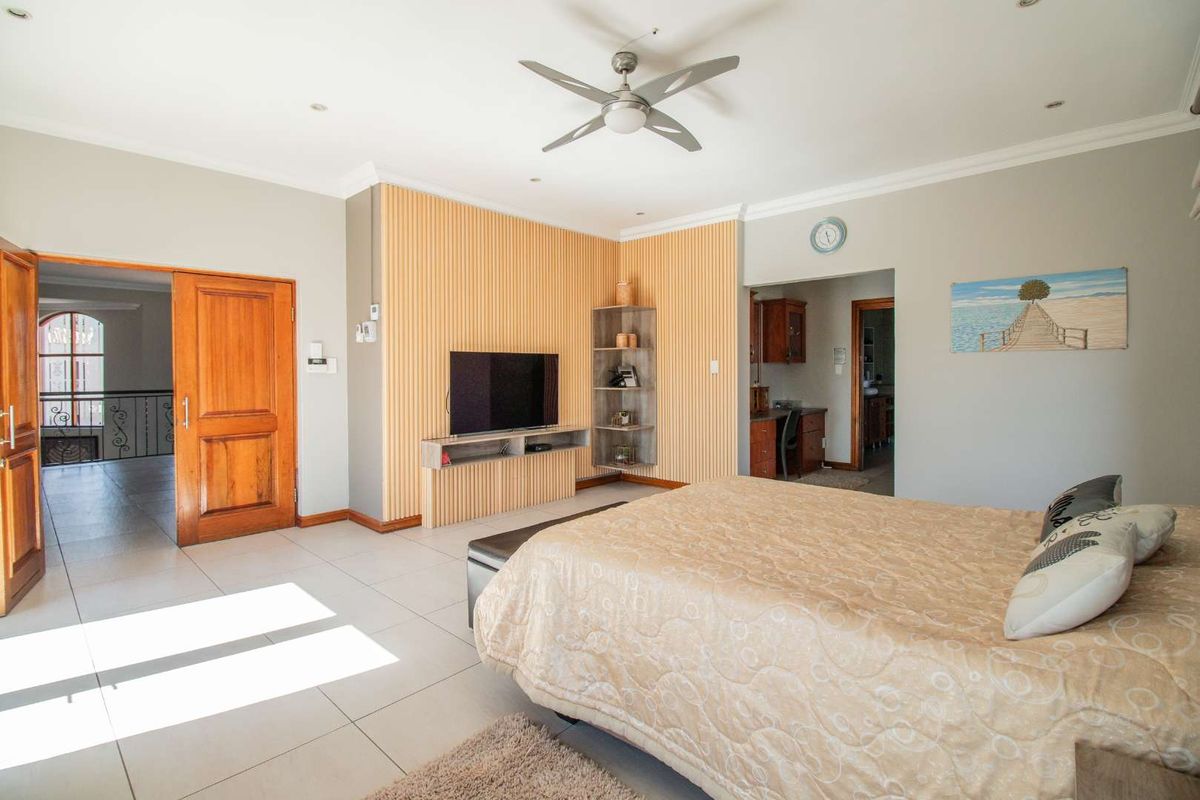 Spacious bedroom featuring tiled flooring, a built-in slatted wood feature wall with integrated shelving, and a ceiling fan.