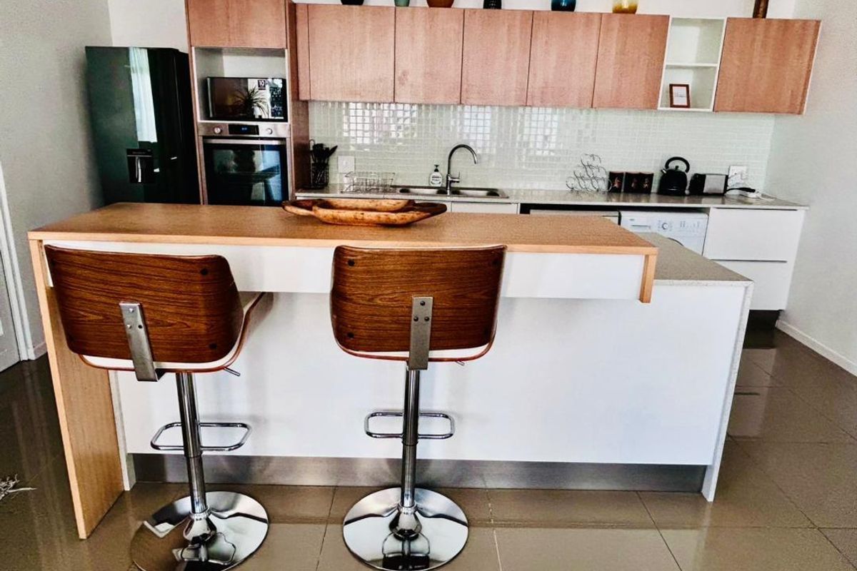 Modern kitchen featuring light wood cabinetry, a breakfast bar island, integrated oven, and tiled backsplash with a double sink.