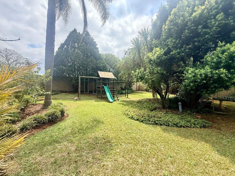 A spacious, well-maintained garden featuring established trees, lush lawn, and a secure boundary wall, providing a private outdoor setting.