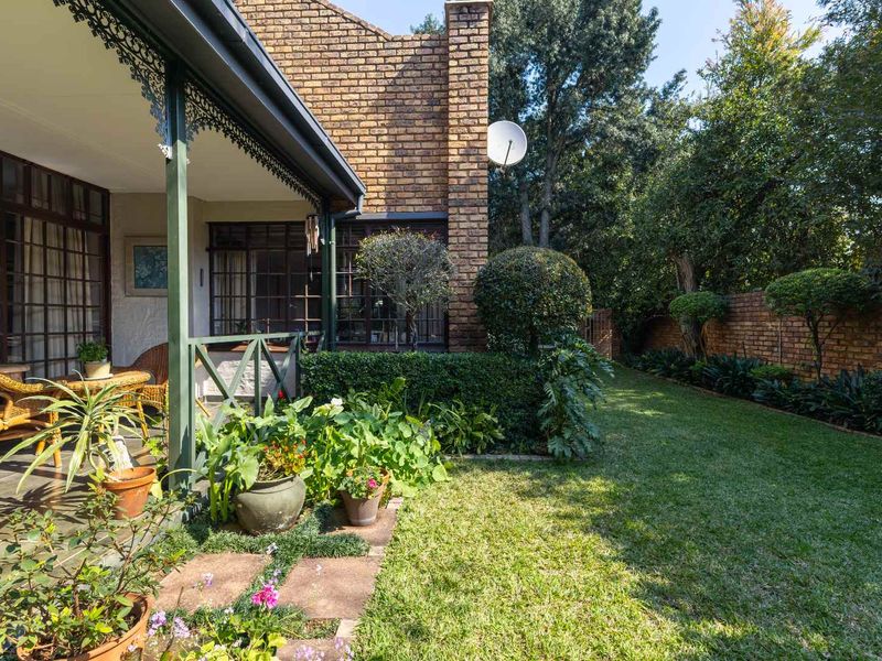 A private rear garden featuring a covered patio with decorative ironwork, established landscaping, and a brick-walled boundary.