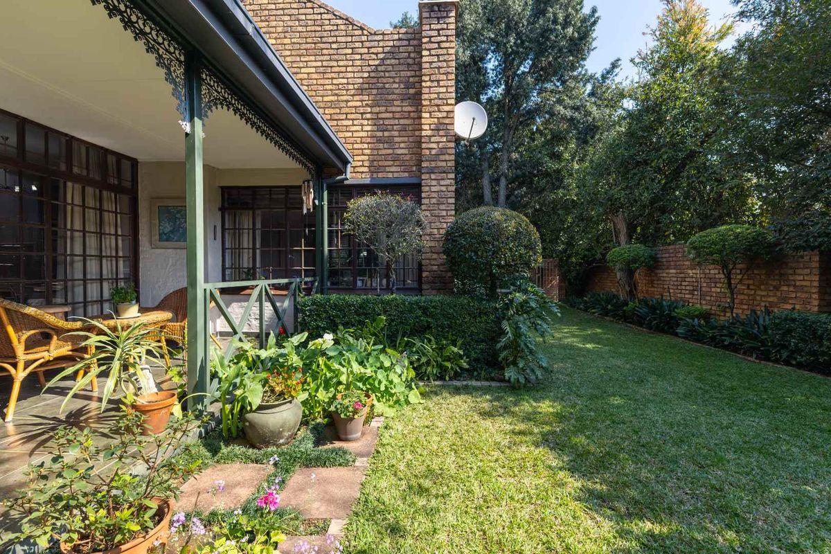 A private rear garden featuring a covered patio with decorative ironwork, established landscaping, and a brick-walled boundary.