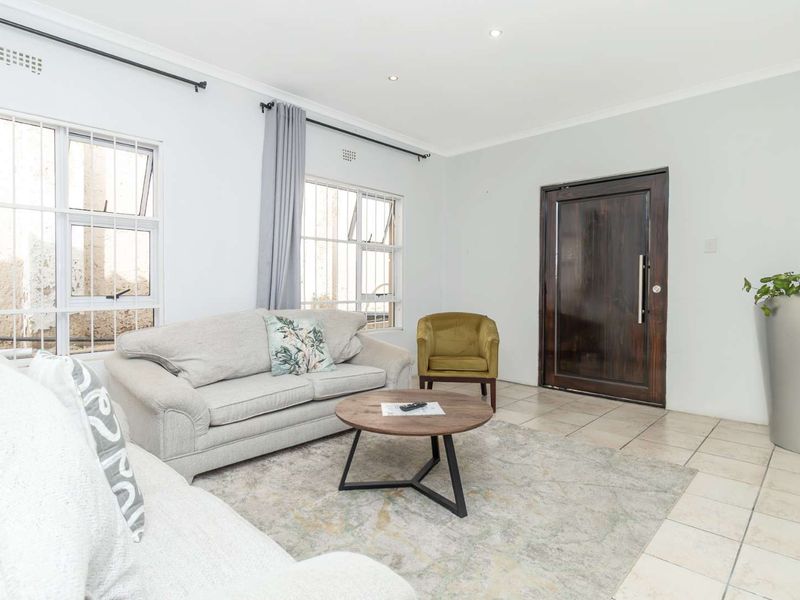 A bright and well-maintained living room featuring tiled flooring, recessed downlighting, and a solid wood entrance door with security-fitted windows.