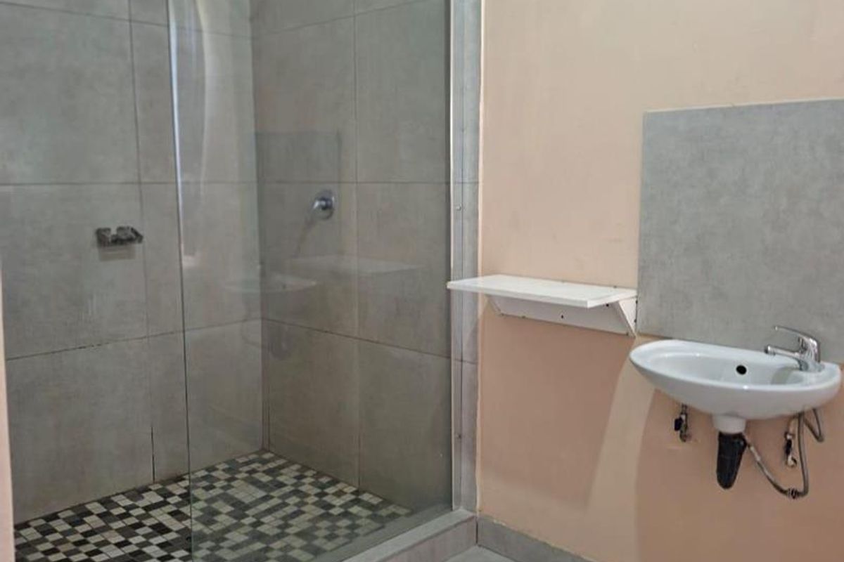 A functional bathroom featuring a glass-enclosed walk-in shower with tiled flooring and a wall-mounted basin.