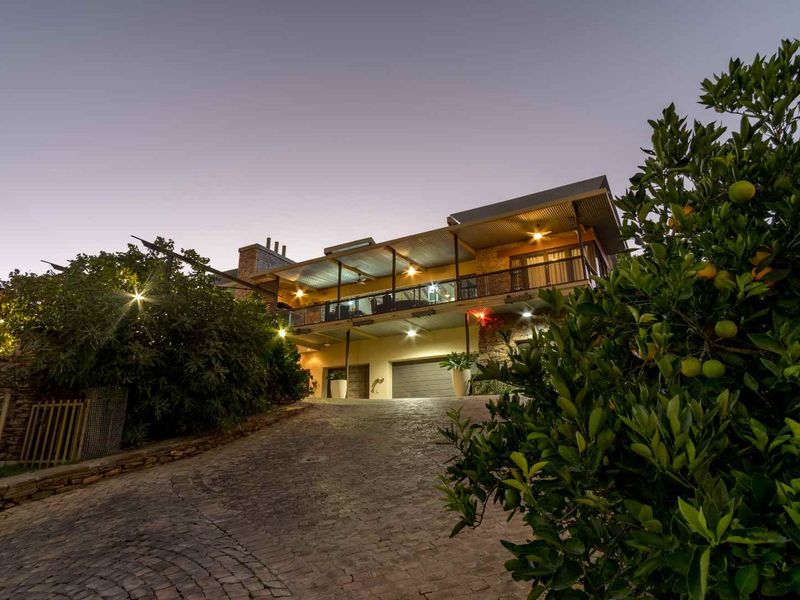 A striking multi-level home exterior at dusk, featuring a cobblestone driveway, double garage, and a spacious covered balcony with stone architectural details.