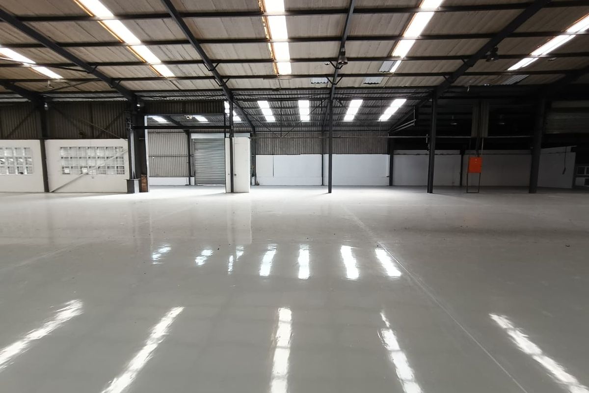 Spacious industrial warehouse featuring a polished epoxy floor, high steel portal frame ceiling with integrated skylights, and a large roller shutter door.