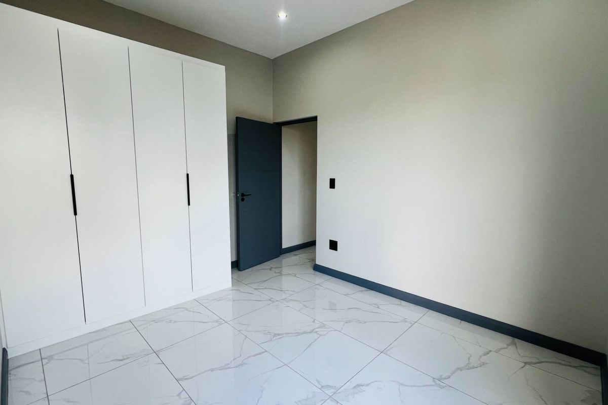 A bright, modern bedroom featuring sleek white built-in wardrobes, high-gloss marble-look floor tiles, and contrasting dark grey door and skirting boards.