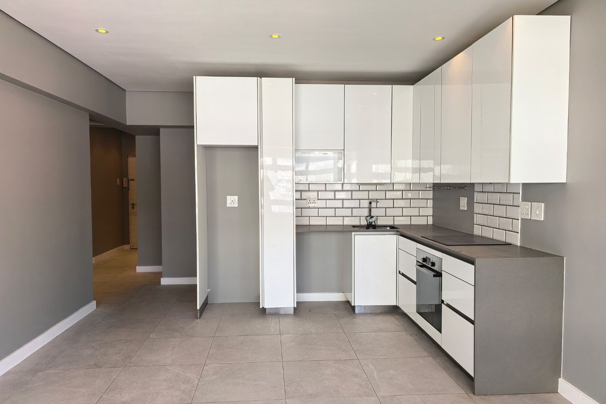 Modern kitchen featuring sleek white cabinetry, grey stone countertops, subway tile backsplash, and integrated appliances in an open-plan layout.