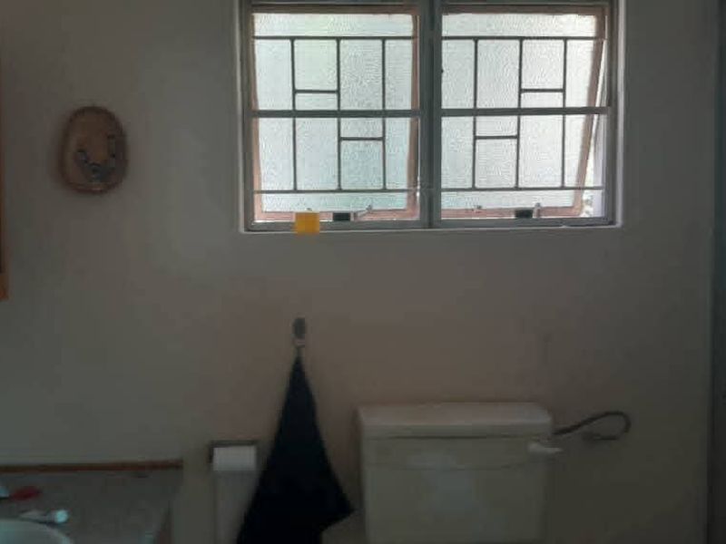 A functional bathroom featuring a vanity, toilet, and shower enclosure with security bars on the window.