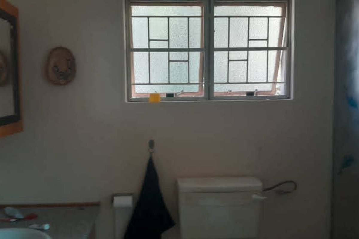 A functional bathroom featuring a vanity, toilet, and shower enclosure with security bars on the window.