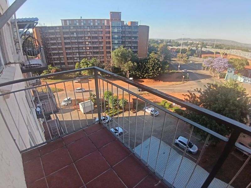 An elevated balcony featuring tiled flooring and a metal safety railing, offering an open view of the surrounding neighborhood and parking area.