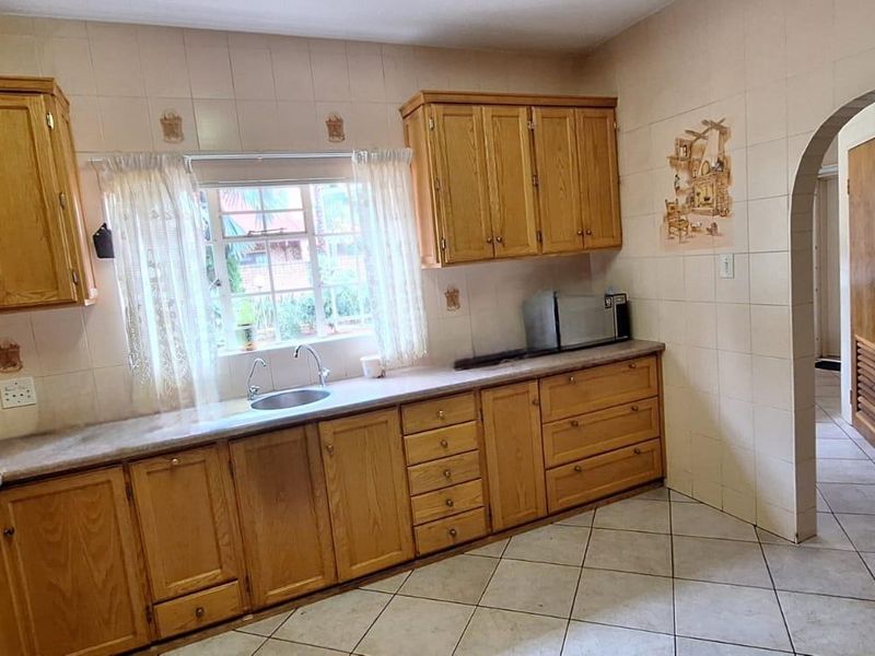 A functional kitchen featuring traditional wooden cabinetry, tiled backsplash, and tiled flooring, offering a classic layout with an arched entrance to the hallway.