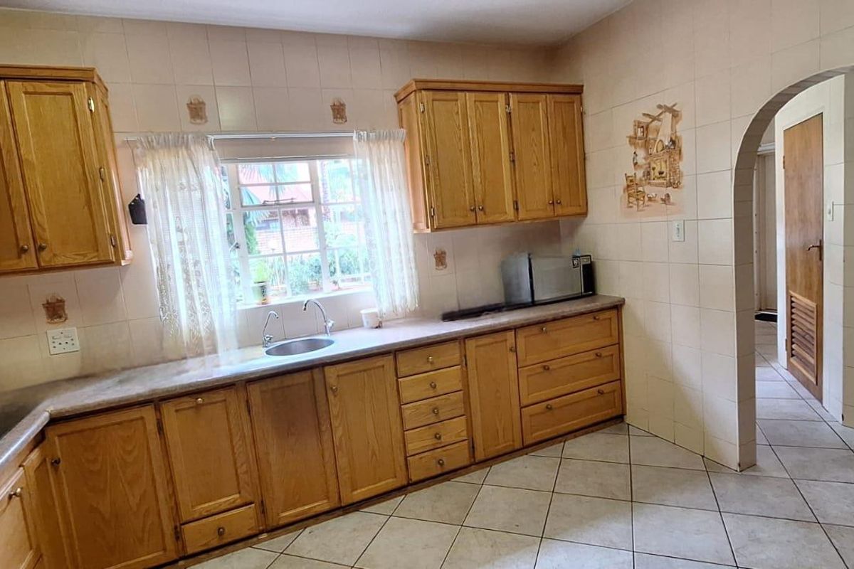 A functional kitchen featuring traditional wooden cabinetry, tiled backsplash, and tiled flooring, offering a classic layout with an arched entrance to the hallway.