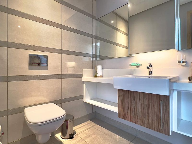 Modern bathroom featuring a wall-mounted toilet with concealed cistern, floating vanity with integrated basin, and large wall-mounted mirror.