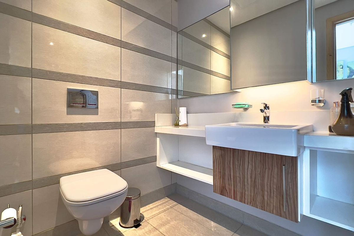 Modern bathroom featuring a wall-mounted toilet with concealed cistern, floating vanity with integrated basin, and large wall-mounted mirror.