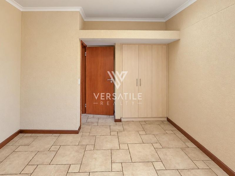 A clean, empty bedroom featuring neutral tiled flooring, built-in cupboards, and a classic wooden door, offering a versatile space ready for personalization.