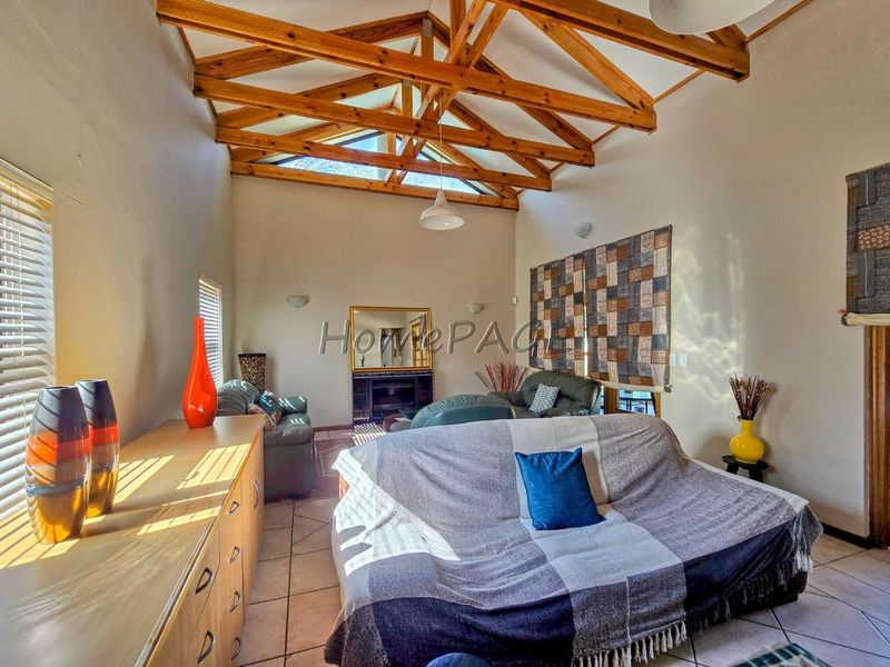 Spacious living room featuring high vaulted ceilings with exposed timber trusses, tiled flooring, and a built-in fireplace.