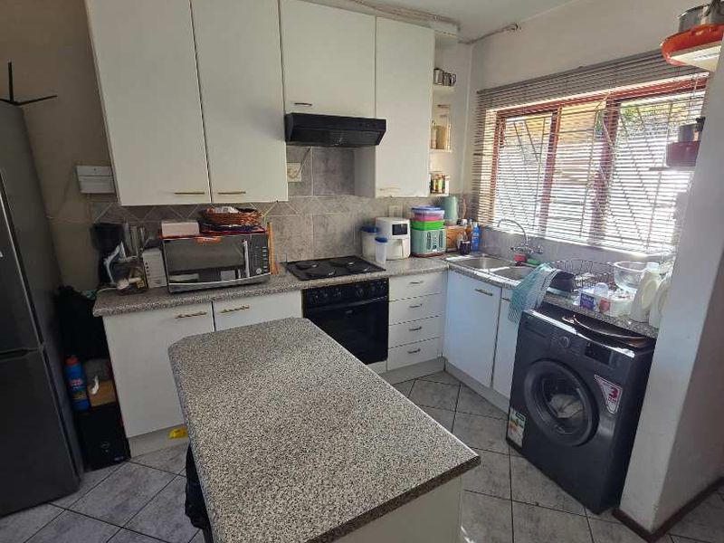 Functional kitchen featuring granite countertops, a central island, built-in oven and hob, and tiled flooring with ample storage cabinetry.