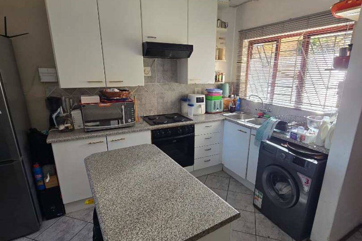 Functional kitchen featuring granite countertops, a central island, built-in oven and hob, and tiled flooring with ample storage cabinetry.