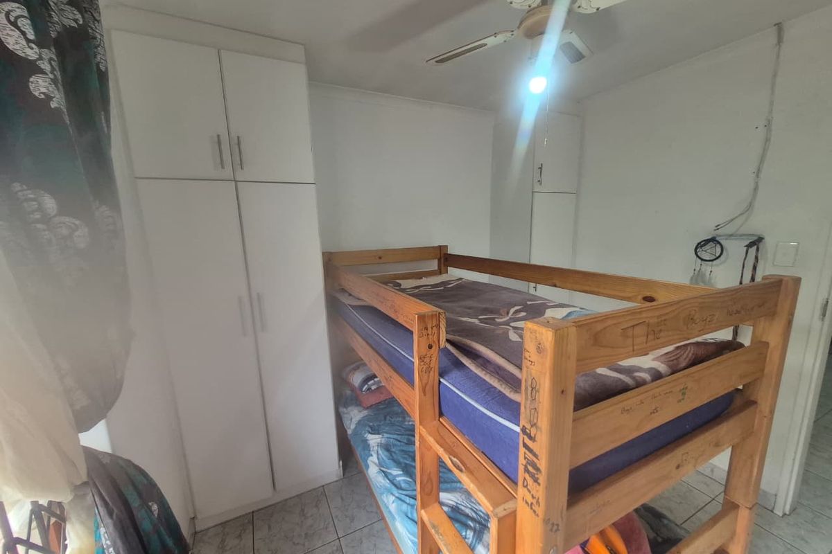 A compact bedroom featuring tiled flooring, built-in white cupboards, and a ceiling fan, requiring minor cosmetic updates to refresh the space.