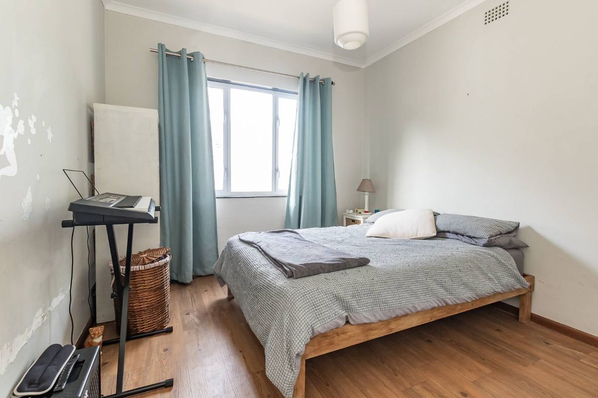 A bedroom featuring wood-look flooring, a window with curtains, and a ceiling light fixture.
