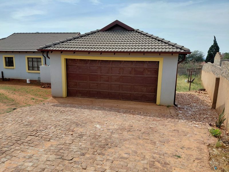A detached garage featuring a tiled roof and a sectional door, set on a cobblestone driveway with surrounding brick boundary walls.