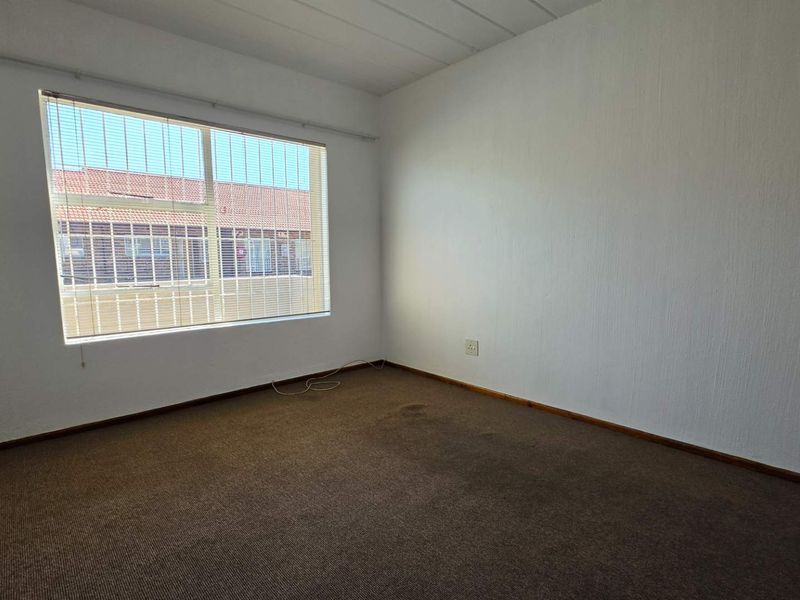 An empty bedroom featuring carpet flooring and a large window with blinds, providing a blank canvas for potential renovation or staging.