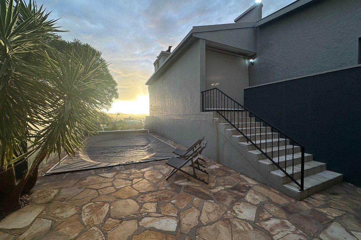 Rear exterior area featuring a paved patio, swimming pool with cover, and an external staircase leading to the upper level of the home.