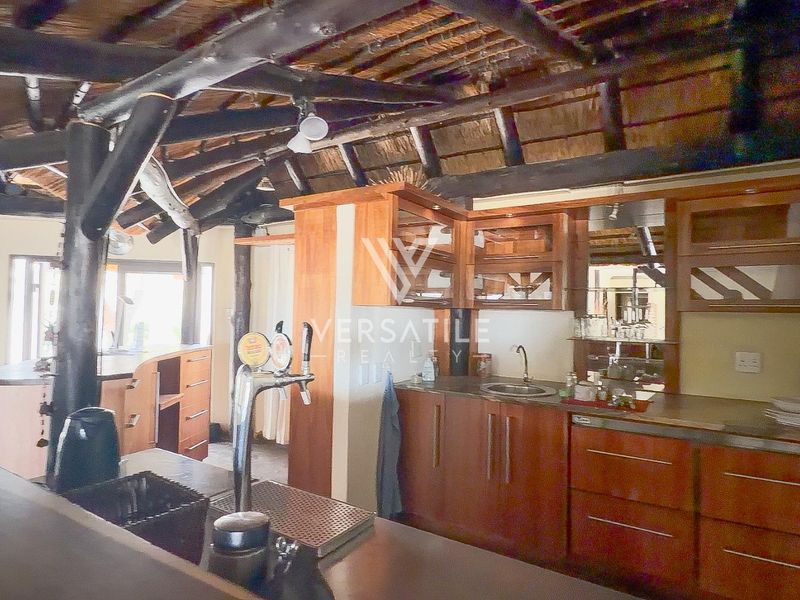 A rustic bar area featuring a traditional thatched roof with exposed timber beams and custom built-in wooden cabinetry with a sink and beer tap.