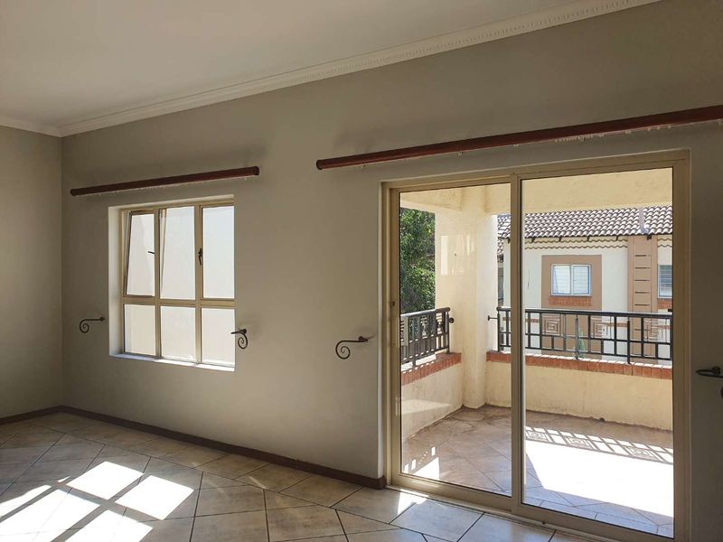 An empty living room featuring tiled flooring, coved ceilings, and a sliding glass door providing access to a private balcony.