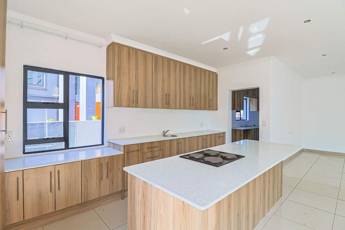Modern kitchen featuring wood-look cabinetry, stone countertops, a central island with an electric hob, and tiled flooring, with an adjacent scullery area.