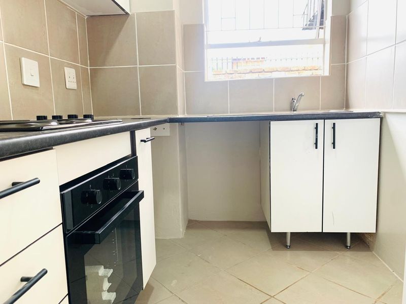 A functional kitchen featuring built-in cabinetry, a hob, an oven, tiled backsplash, and tiled flooring with a window providing natural light.
