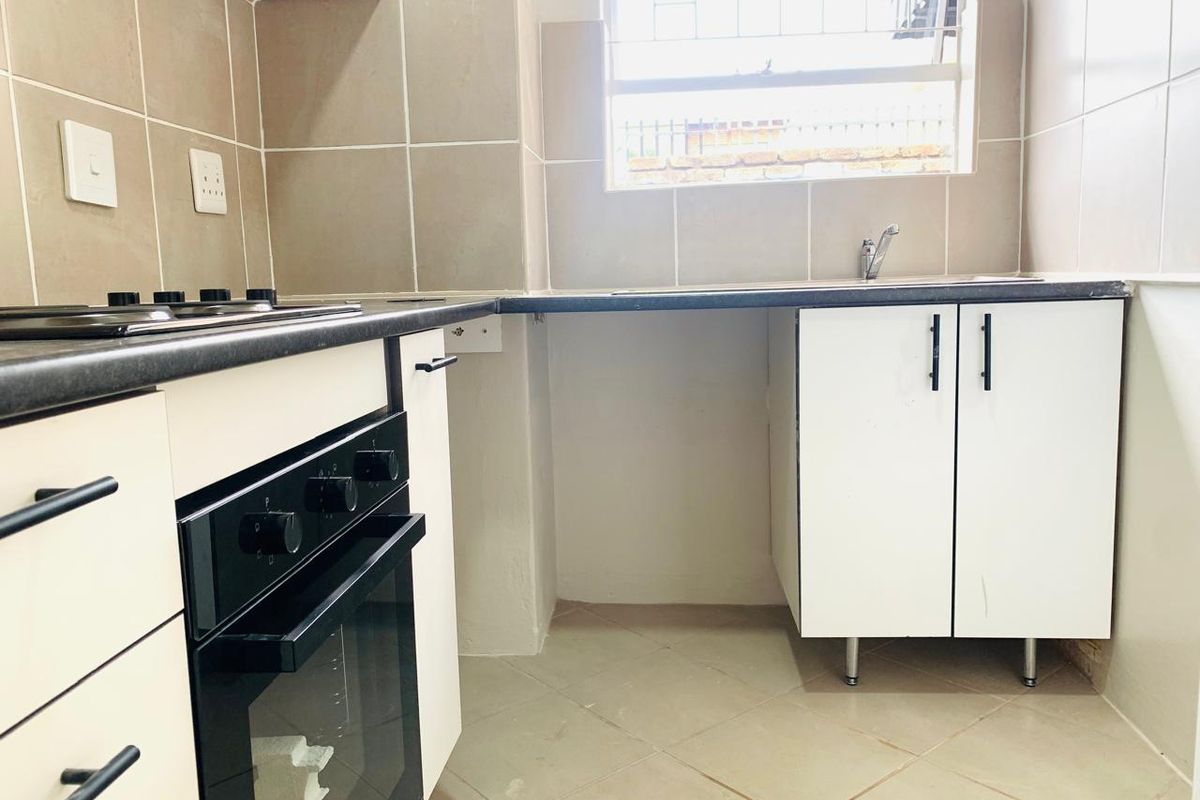 A functional kitchen featuring built-in cabinetry, a hob, an oven, tiled backsplash, and tiled flooring with a window providing natural light.