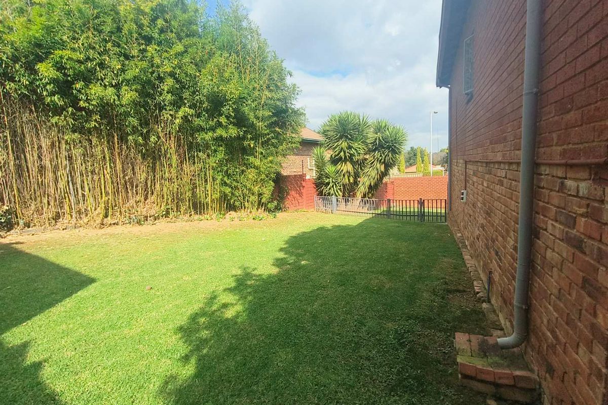 A private rear garden featuring a well-maintained lawn, established bamboo screening, and a brick exterior wall with a functional downpipe.