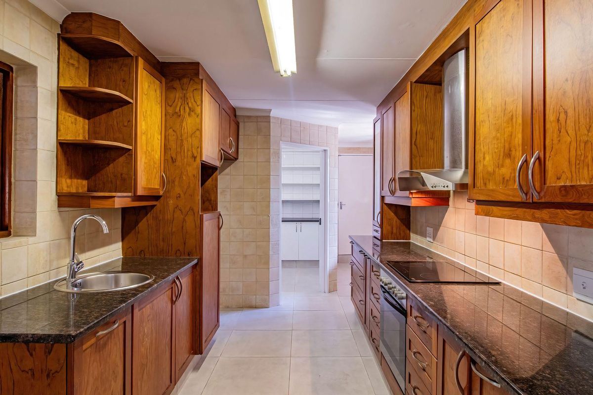 A galley-style kitchen featuring dark granite countertops, wooden cabinetry, a built-in oven, hob, and extractor fan, with an adjacent scullery area.