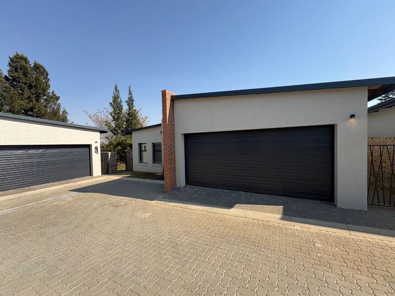 Front view of the property featuring a paved driveway and two modern sectional garage doors with a textured plaster finish.