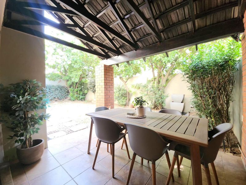 A covered patio area featuring tiled flooring, a brick support pillar, and an exposed timber beam ceiling, overlooking a private garden space.