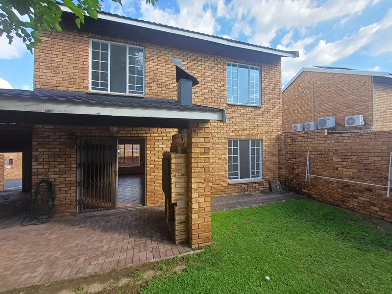 Rear view of a brick townhouse featuring a covered patio with a built-in braai, paved area, and a small private garden.