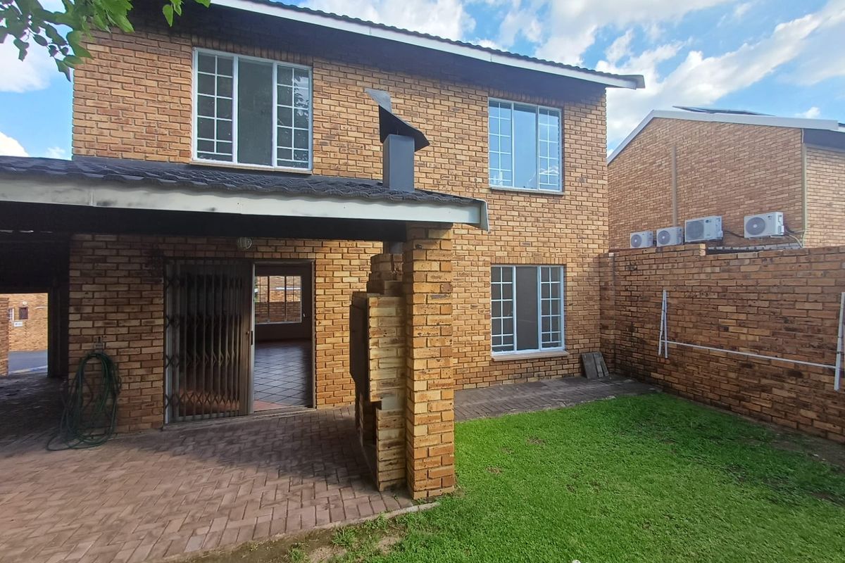 Rear view of a brick townhouse featuring a covered patio with a built-in braai, paved area, and a small private garden.