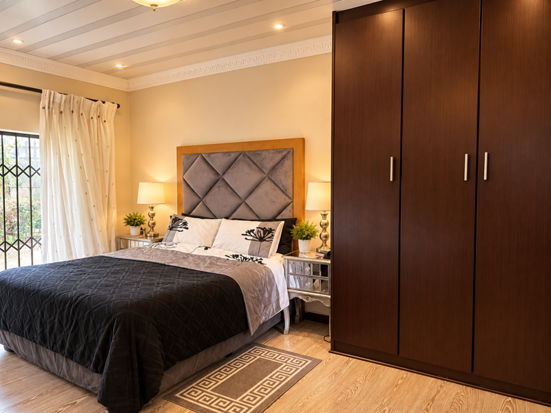 A well-maintained bedroom featuring a large built-in wardrobe, recessed ceiling lighting, decorative crown molding, and a security gate on the window.