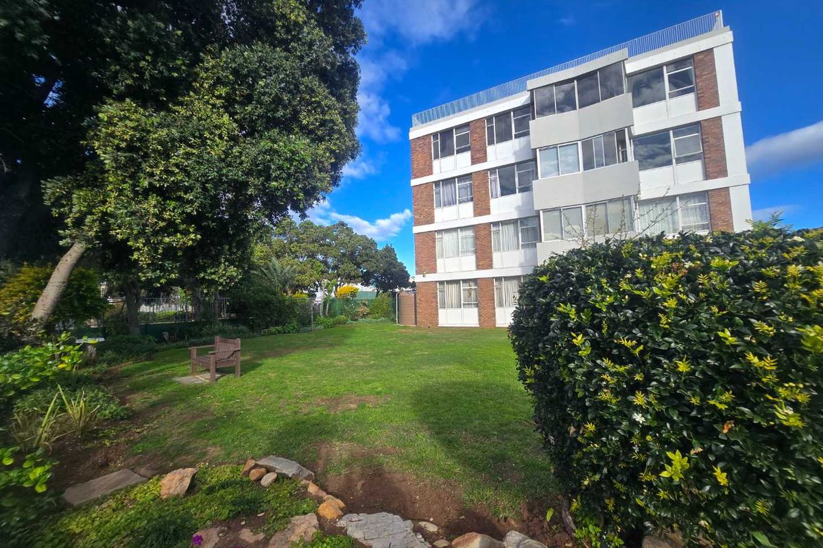 A view of the rear apartment building facade featuring a well-maintained lawn and landscaped garden area.