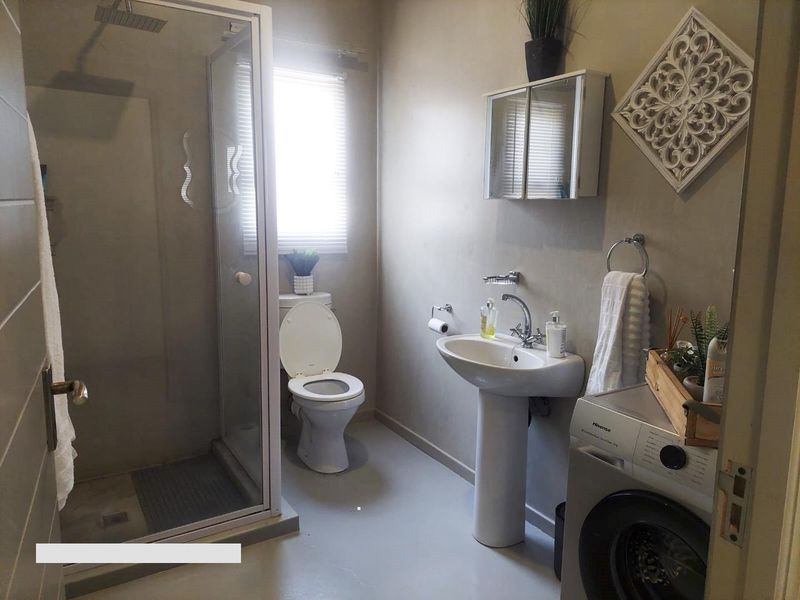 A functional bathroom featuring a pedestal basin, a glass-enclosed shower, and a toilet, with neutral wall finishes and integrated laundry space.