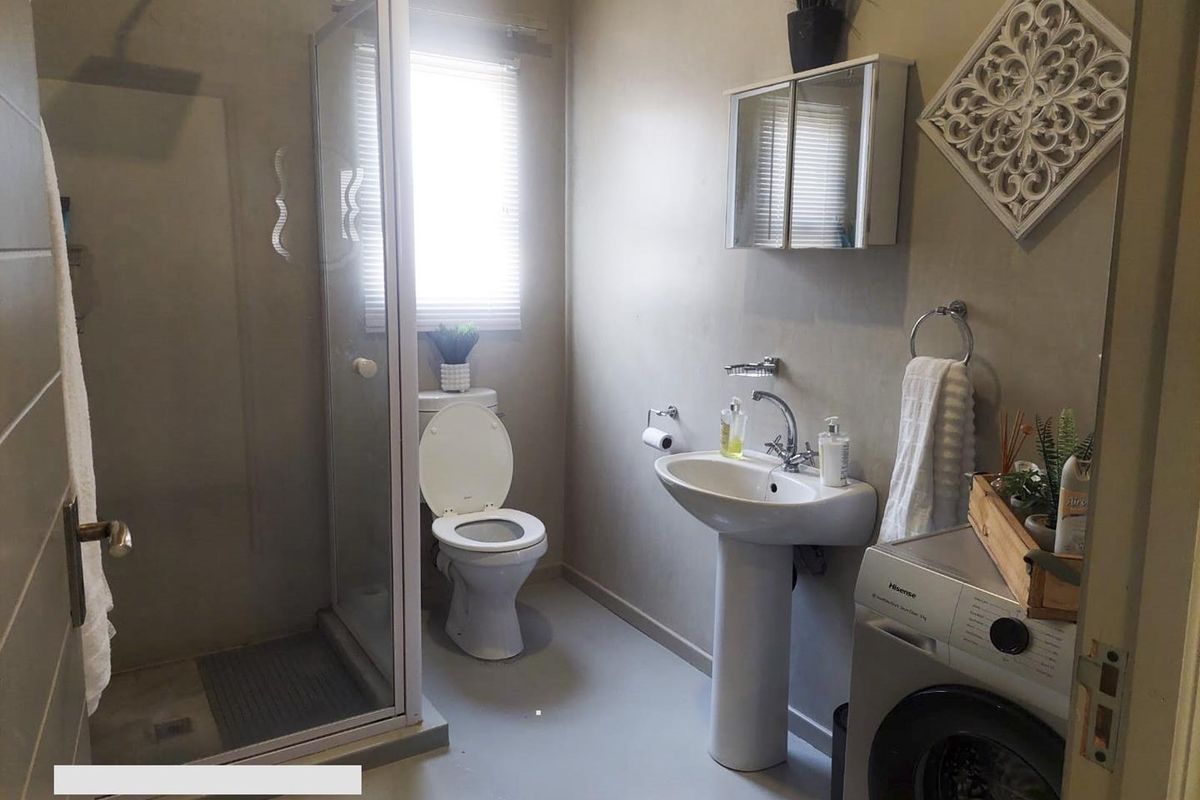 A functional bathroom featuring a pedestal basin, a glass-enclosed shower, and a toilet, with neutral wall finishes and integrated laundry space.
