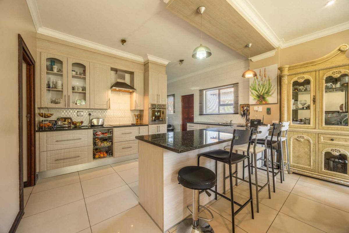 Modern kitchen featuring light wood cabinetry, granite countertops, a central island with breakfast bar seating, and integrated appliances under a decorative ceiling feature.
