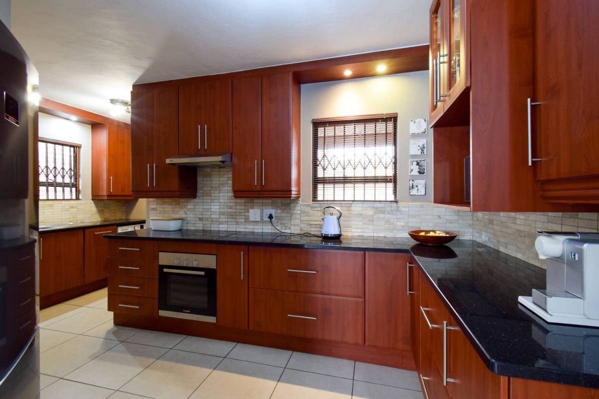 A well-maintained kitchen featuring cherry wood cabinetry, dark granite countertops, a built-in oven, extractor fan, and tiled backsplash with recessed lighting.