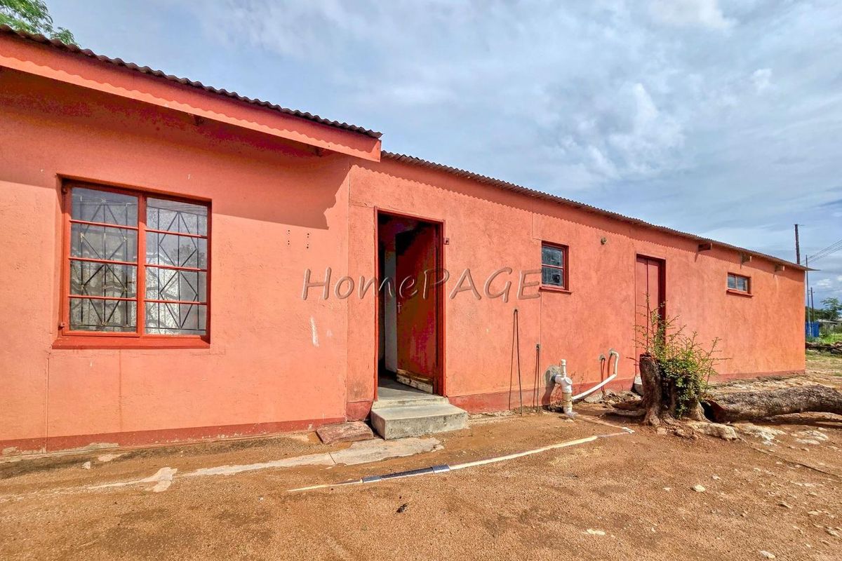Rear exterior view of a single-story house featuring a simple facade, metal window frames with security bars, and exposed exterior plumbing.