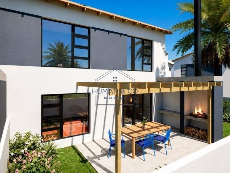 Rear exterior view of the townhouse featuring a paved patio with a wooden pergola and a built-in braai area overlooking a private garden.