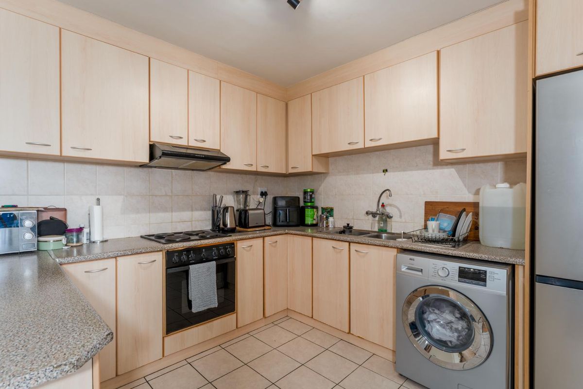 Functional kitchen featuring light wood-finish cabinetry, granite-look countertops, tiled backsplash, built-in oven with hob, extractor fan, and integrated space for a washing machine.